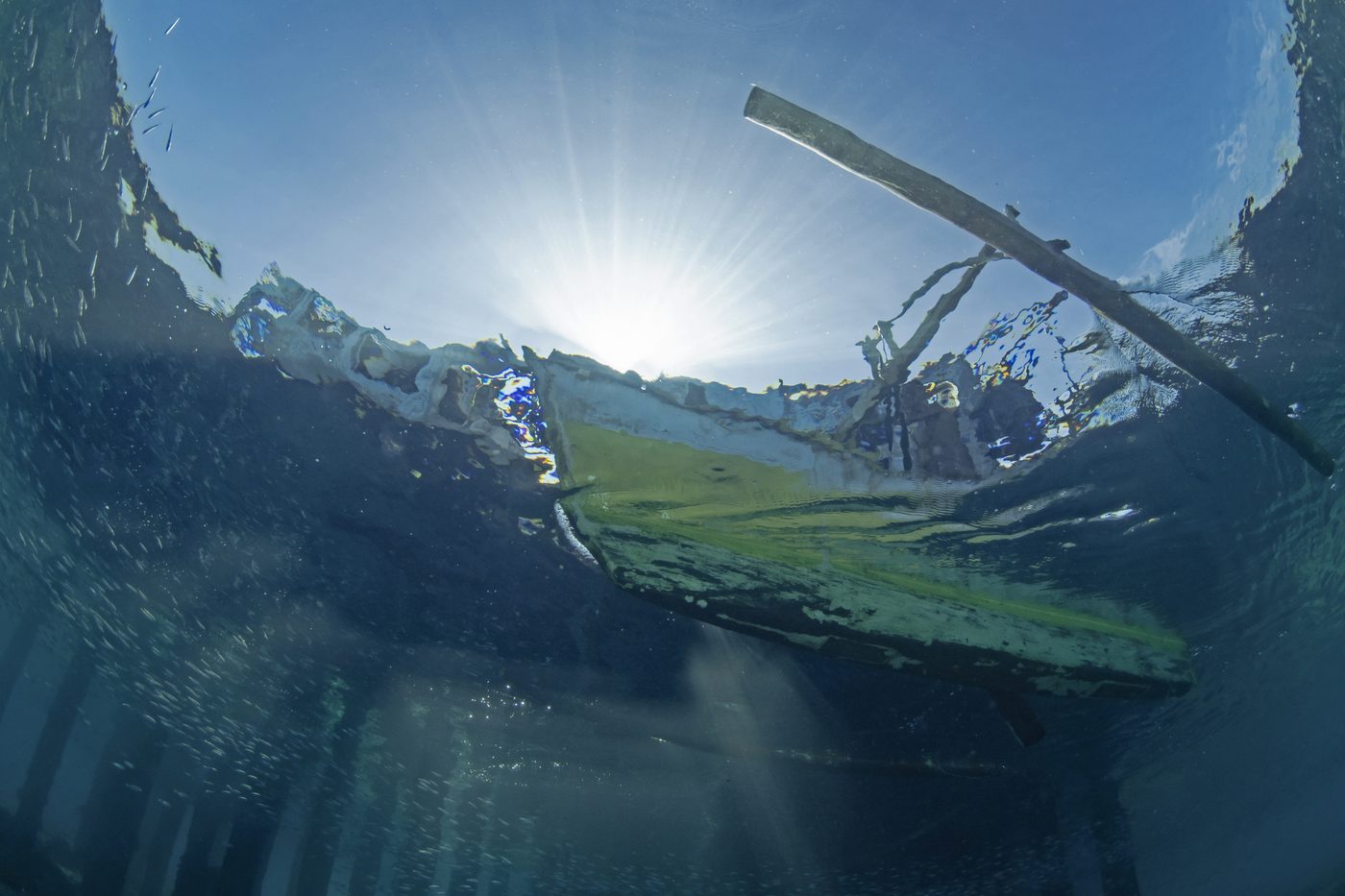 An outrigger canoe viewed from beneath the ocean surface.